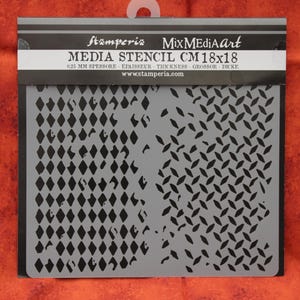 May include: A gray stencil with a repeating diamond pattern and the text "Stamperia Mix Media Art Media Stencil CM18x18". The stencil measures 18 cm x 18 cm.