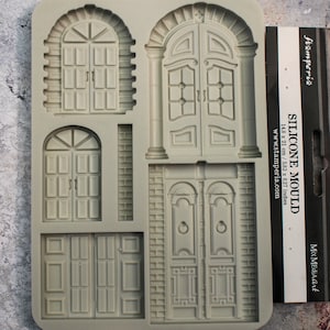 Op de afbeelding: Een grijze siliconen mal met gedetailleerde architecturale deurontwerpen. De mal bevat verschillende deur stijlen, zoals gewelfde en rechthoekige, met ingewikkelde panelen en hardware. De verpakking aan de rechterkant leest "SILICONE MOULD" en meet 14,8 x 21 cm.