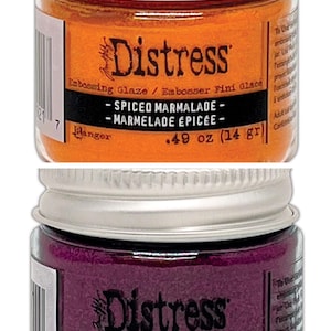 Op de afbeelding: Twee kleine potjes Distress Embossing Glaze. De bovenste pot is oranje en heeft het label "Spiced Marmalade - Marmelade &Eacute;pic&eacute;e - 0,49 oz (14 g)". De onderste pot is paars en heeft het label "Seedless Preserves - Raisin en Conserves - 0,49 oz (14 g)".
