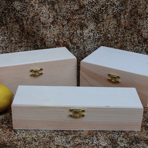 May include: Three wooden boxes with lids and gold latches. The boxes are different sizes and are arranged in a row on a brown textured surface.
