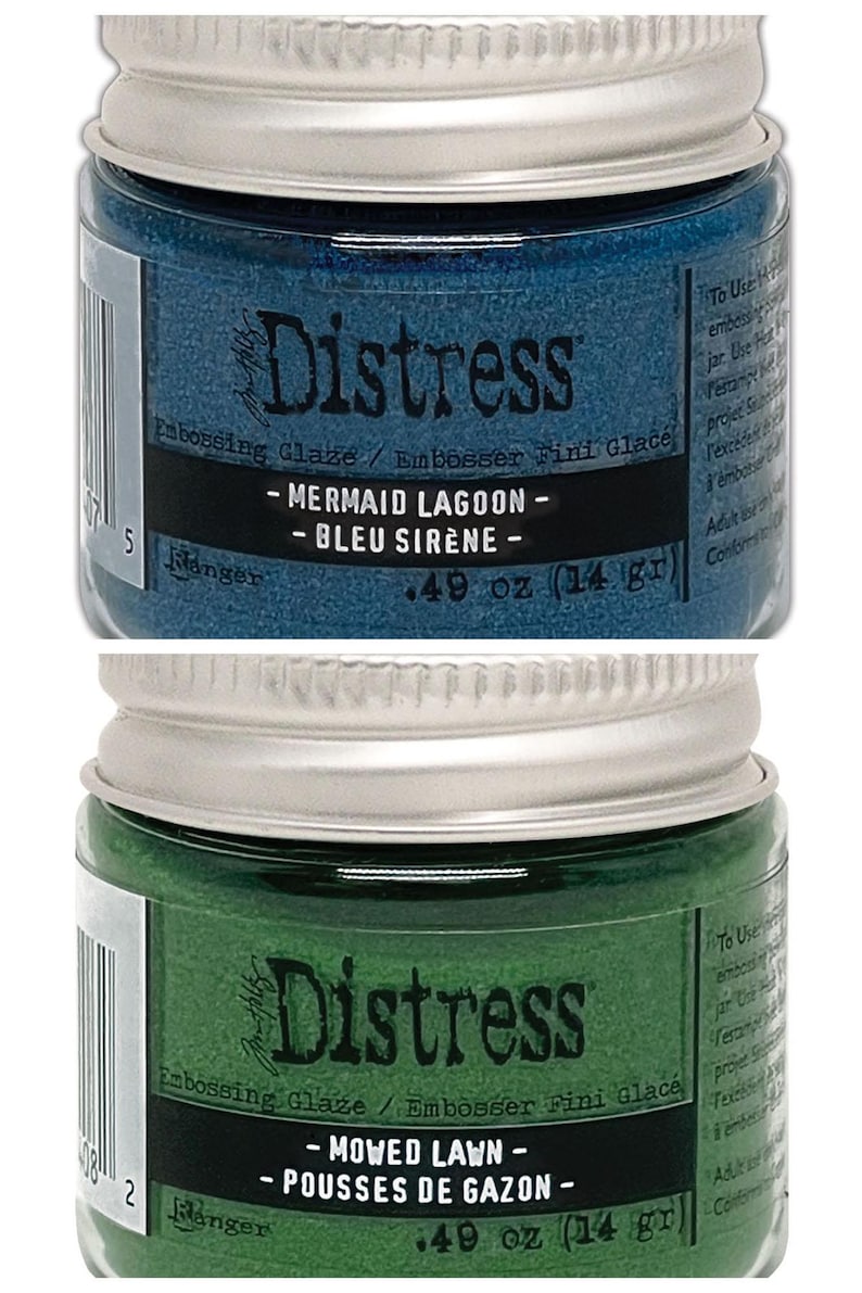 Op de afbeelding: Twee kleine potjes Distress Embossing Glaze. De bovenste pot is blauw en heeft het label "Mermaid Lagoon - Bleu Sir&egrave;ne - 0,49 oz (14 gr)". De onderste pot is groen en heeft het label "Mowed Lawn - Pousses de Gazon - 0,49 oz (14 gr)".