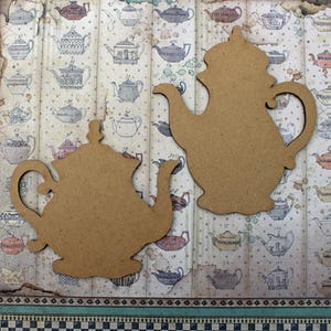 May include: Two unfinished wooden teapots, one with a traditional design and the other with a more ornate design. The teapots are on a background of a vintage teacup pattern.