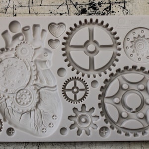 May include: A silicone mold for baking with a design of a heart with gears and other gears and hearts.