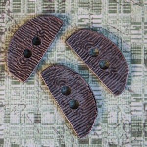 May include: Three brown, half-circle buttons with a textured surface and two holes each.