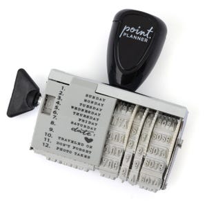 May include: A black and silver date stamp with the text "point. PLANNER" on the top. The stamp includes the days of the week and the word "date:" with a heart symbol. The stamp is designed for marking dates.