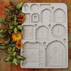 May include: A white silicone mold featuring various miniature door and window designs, including arched doorways, rectangular doors, and round windows. The mold is decorated with a floral arrangement of yellow and orange flowers and green leaves.
