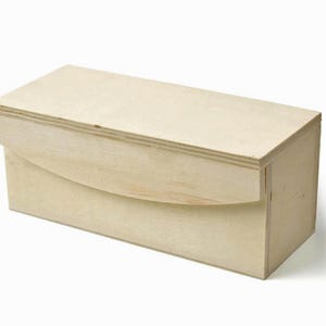 May include: A rectangular wooden box with a curved, hinged lid. The box is made of light-colored wood and has a simple, clean design. The lid curves down on one side, creating a unique shape. The box is likely used for storage or display.