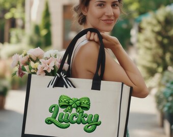 Może przedstawiać: Płócienna torba typu tote w kolorze kremowym z czarnymi uchwytami i czarnym spodem. Torba ma napis "Lucky" w zielonym kolorze z zieloną kokardą. Torba jest wypełniona różowymi i białymi kwiatami.