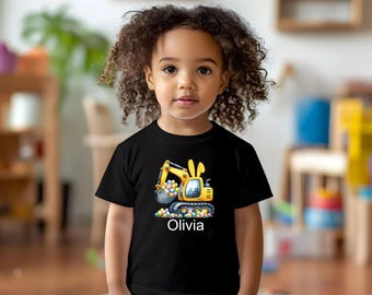 Może przedstawiać: Czarny t-shirt z żółtą koparką z króliczymi uszami, zbierającą kolorowe pisanki. Imię "Olivia" jest wydrukowane na biało. Dziecko ma na sobie koszulkę.