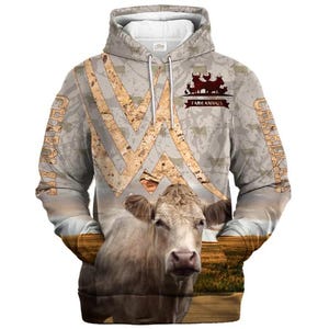 May include: A beige hooded sweatshirt featuring a large, realistic cow graphic on the front, a field landscape, and a textured pattern of cattle silhouettes. The text "FARM ANIMALS" and "CHAROLAIS" are printed on the garment in a dark brown font.