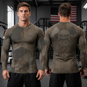 May include: A long-sleeve compression shirt featuring a brown and olive green camouflage pattern. The front displays a stylized stone-like face graphic on the chest, while the back features a larger version of the same graphic and a star icon.