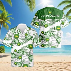 Può includere: Camicia bianca con bottoni con un motivo floreale e a foglie tropicali, con il logo John Deere. La camicia ha un colletto verde e le parole "John Deere" stampate sul retro. Il design include colori verdi e bianchi.
