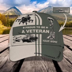 Puede incluir: Gorra de béisbol con temática militar, principalmente blanca y verde oliva. Presenta un helicóptero, tanques y el texto "PROUD TO BE A VETERAN". También incluye espacio para un nombre personalizado y las palabras "HONOR - COURAGE - COMMITMENT".