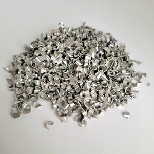 Könnte beinhalten: Ein Haufen glänzender, silberner Metallspäne. Die Späne sind eng gerollt und haben ein strukturiertes Aussehen. Das Metall scheint frisch geschnitten zu sein, mit einer hellen, reflektierenden Oberfläche. Der Haufen befindet sich auf weißem Hintergrund.