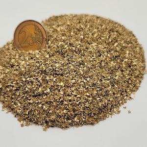Può includere: Un mucchio di piccoli pezzi di metallo dorato, possibilmente decorativi o per l'artigianato, con una moneta da due euro per la scala. La moneta è color bronzo e mostra il numero 2. I pezzi di metallo hanno un aspetto strutturato e organico.
