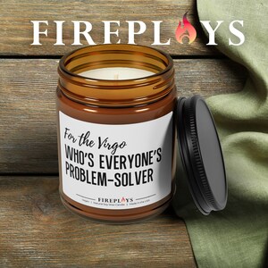 May include: A brown glass jar candle with a black lid, featuring the text "For the Virgo Who's Everyone's Problem-Solver." The candle has a white label and a lit wick. The brand name "FIREPLOYS" is at the top.