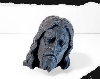 May include: A dark gray sculpture of a head with long hair and a beard, with the text "FALLEN GOD" above it. The sculpture has a weathered appearance with cracks and crevices. The bottom right corner features the "KEEP DESIGN" logo.