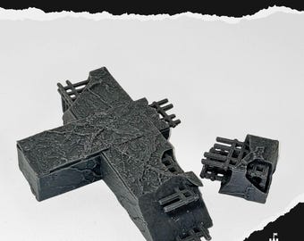 May include: A dark gray, weathered concrete cross with the text "FALLEN CONCERTE CROSS". The cross is broken and has a textured surface. A smaller, detached piece of the cross is also present.