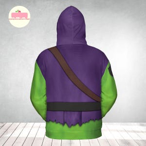 May include: A hooded sweatshirt with a purple body, green sleeves, and a brown strap across the back. The bottom hem has a jagged edge, and a black belt is visible. The design is reminiscent of a costume.