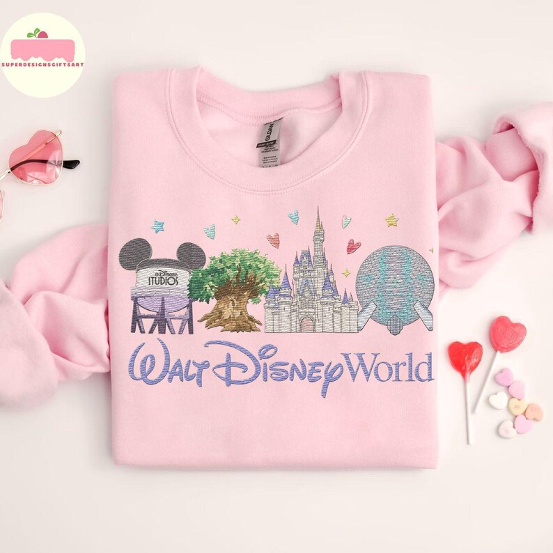 May include: A pale pink sweatshirt with an embroidered design of Walt Disney World landmarks, including the Hollywood Studios water tower, the Tree of Life, Cinderella Castle, and Spaceship Earth. The words "Walt Disney World" are embroidered in a script font.