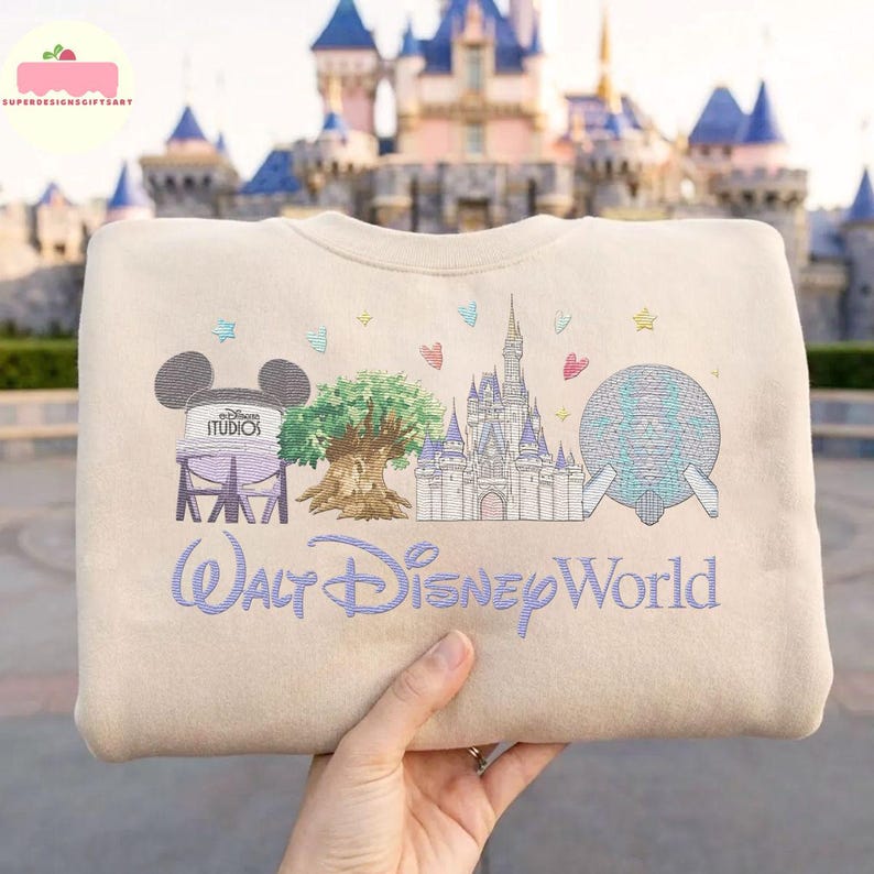 May include: Beige sweatshirt with embroidered Walt Disney World design. Features Mickey Mouse ears, a tree, a castle, and a sphere. The text "Walt Disney World" is embroidered in a cursive font.