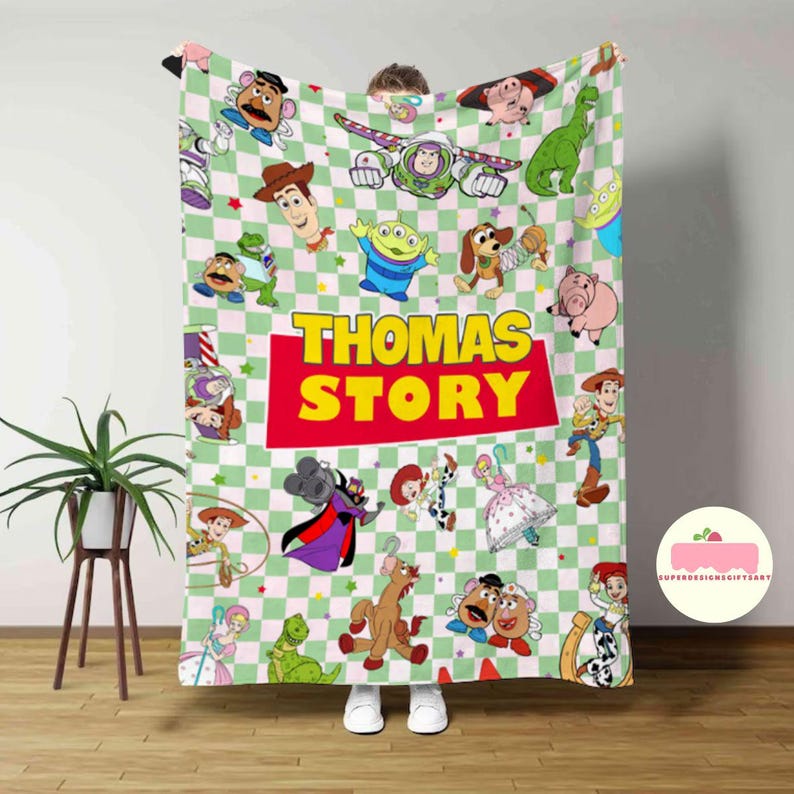 May include: A personalized blanket featuring characters from the Toy Story movie franchise. The blanket has a green and white checkered pattern with various character illustrations. The name "THOMAS STORY" is prominently displayed in yellow letters on a red background.