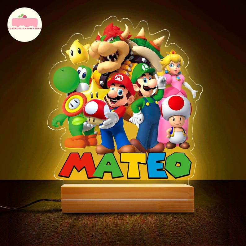 Peut inclure: Lampe de chevet LED color&eacute;e repr&eacute;sentant des personnages de Super Mario, dont Mario, Luigi et la Princesse Peach. Le nom "MATEO" est affich&eacute; en grandes lettres color&eacute;es. La lampe est pos&eacute;e sur une base en bois.