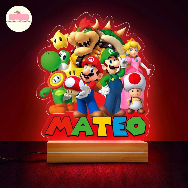 Peut inclure: Une veilleuse LED rouge repr&eacute;sentant une illustration color&eacute;e de Mario, Luigi et d'autres personnages de la s&eacute;rie de jeux vid&eacute;o Super Mario Bros. Le nom "MATEO" est affich&eacute; en grandes lettres color&eacute;es. La lumi&egrave;re repose sur une base en bois.