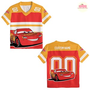 May include: A red and yellow short-sleeved jersey featuring Lightning McQueen from the Cars movie. The jersey has white stripes and the number "00" on the back, with the text "CUSTOM NAME" above it. The front features a large graphic of Lightning McQueen.