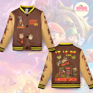 May include: Brown and tan varsity jacket featuring Donkey Kong 64 graphics. The jacket has a yellow collar and cuffs with black stripes. The back of the jacket says "IT IS ON LIKE GAME OVER DONKEY KONG".