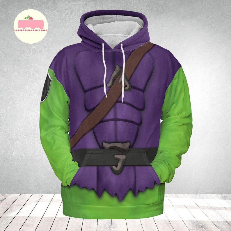 May include: A hooded sweatshirt featuring a purple and green design, with a brown strap across the chest. The sleeves are green, and the body of the sweatshirt is purple with a black belt and a green hem. The design resembles a costume.