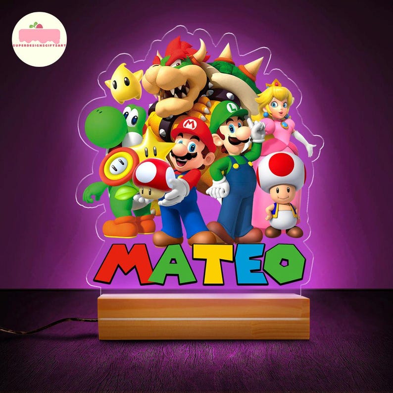 Peut inclure: Lampe de chevet LED color&eacute;e avec des personnages de Super Mario Bros. Mario, Luigi, et la Princesse Peach sont repr&eacute;sent&eacute;s. Le nom "MATEO" est affich&eacute; en couleurs vives. La base est en bois.
