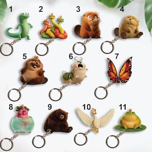 May include: A collection of eleven cartoon character keychains. The keychains feature various animals and creatures, including a green lizard, a brown bear, a frog, a butterfly, and a goose. Each keychain is attached to a silver metal ring.