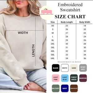 May include: A beige embroidered sweatshirt size chart with measurements in inches. The chart lists sizes XS to 6XL, body length from 63.5 to 86.4 cm, and body width from 45.7 to 91.4 cm. Color options include black, white, sand, sport grey, light pink, light blue, forest green, maroon, military, navy, and chocolate.