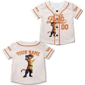 May include: White baseball jersey with orange pinstripes and trim. Features the text "Puss in Boots" and a cartoon image of the character. The jersey also has the number "00" and the text "Your Name" on the back.
