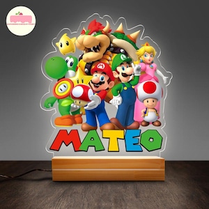 Peut inclure: Une veilleuse en acrylique color&eacute;e repr&eacute;sentant les personnages de la franchise de jeux vid&eacute;o Super Mario Bros. La lumi&egrave;re comprend Mario, Luigi, la princesse Peach et d'autres personnages, avec le nom "MATEO" en grandes lettres color&eacute;es &agrave; la base. La lumi&egrave;re repose sur une base en bois.