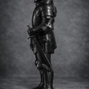 May include: A full suit of black medieval armor, including a helmet, chest plate, arm and leg protection, and boots. The armor is highly detailed and appears to be made of metal. A sword is held at the ready. The Medieval Store logo is in the upper right corner.