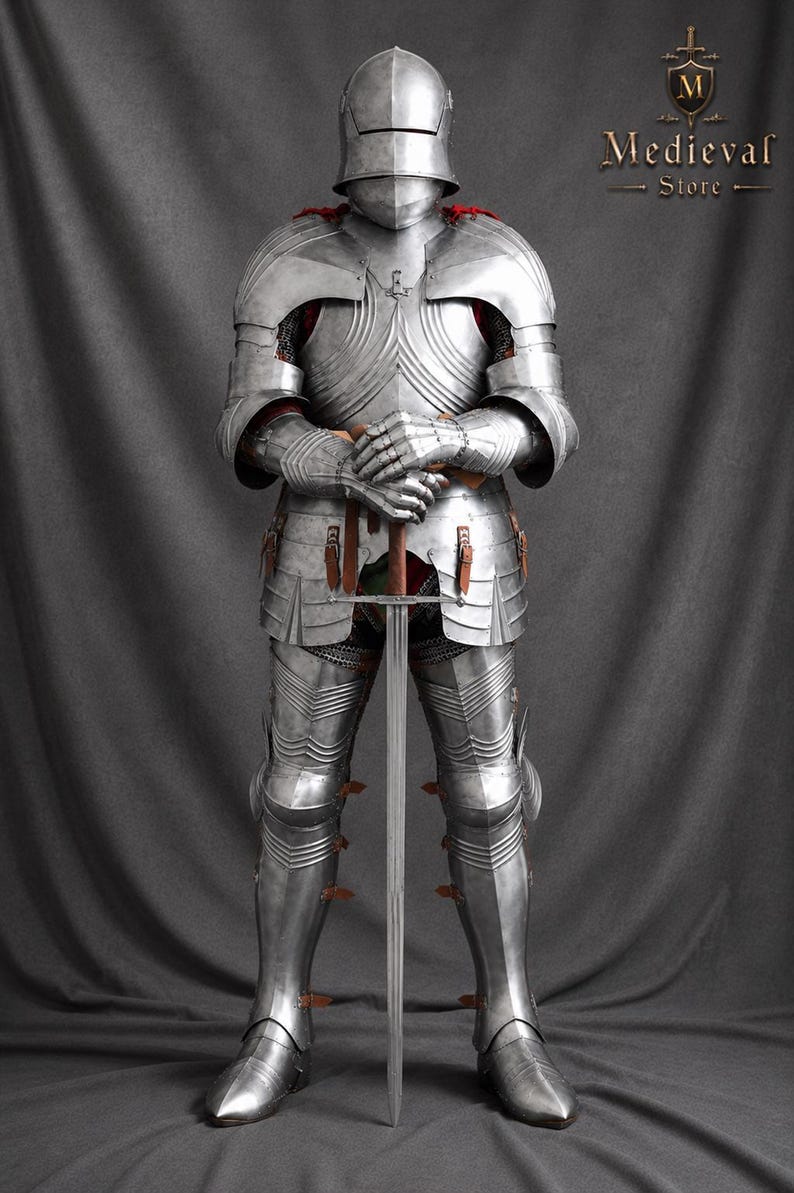 Handmade medieval full plate knight armor suit crafted from polished steel, featuring a Gothic-style helmet, articulated body armor, gauntlets, leg armor, and leather straps, displayed holding a medieval sword against a gray backdrop.