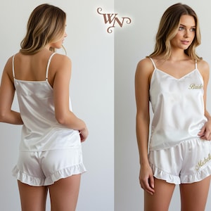 May include: White satin pajama set with a camisole top and ruffled shorts. The top has thin straps and the word "Bride" embroidered in gold. The shorts are also embroidered with a name in gold. A perfect gift for a bride.