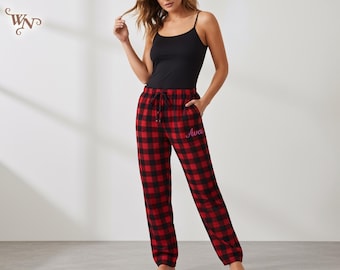 May include: Black camisole top paired with red and black plaid pajama pants. The pajama pants have a drawstring waist and the name "Ava" embroidered in pink. The pants are a classic buffalo check pattern.