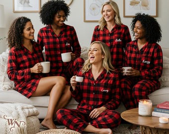 May include: A group of people wearing matching red and black plaid pajama sets, each holding a white mug. The pajamas have personalized names embroidered on them. A candle and books are on a nearby table.