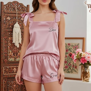 Könnte beinhalten: Ein Schlafanzug-Set aus altrosa Satin, bestehend aus einem ärmellosen Top mit Bindeträgern und passenden Shorts. Das Top ist mit dem Wort Bae in schwarzer Schreibschrift bedruckt, und auf dem Bein der Shorts steht der Name Eva in schwarzer Schrift.