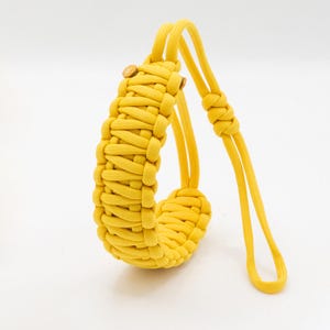 May include: A bright yellow, hand-woven paracord wrist strap with a loop. The strap features a braided design and wooden button accents. The strap is designed to be worn around the wrist.
