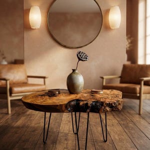 May include: A live edge wood coffee table with a natural grain pattern and dark, textured bark edges, supported by four thin black metal hairpin legs. A ceramic vase containing a dried lotus seed pod sits on the center of the tabletop.