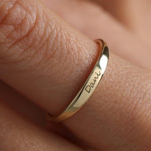 Può includere: Un anello color oro con il nome "Dani" inciso all'esterno. L'anello è sottile e liscio e viene indossato su un dito. L'anello è un gioiello semplice ed elegante.