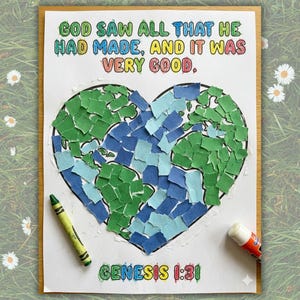 May include: A colorful artwork featuring a heart-shaped collage of green and blue paper pieces, resembling a map. The text "GOD SAW ALL THAT HE HAD MADE, AND IT WAS VERY GOOD" is written above the heart. The text "GENESIS 1:31" is written below the heart. A green crayon and glue stick are on the artwork.