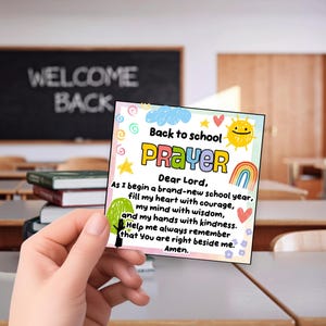 May include: A square card featuring the text Back to school PRAYER and a prayer for the school year. The design includes colorful illustrations of a sun, a rainbow, a tree, stars, and swirls on a white background with a light pink border.