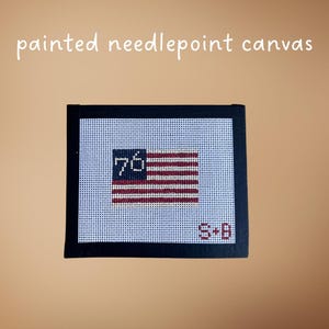 May include: Painted needlepoint canvas featuring a stylized American flag design. The flag has red and white stripes, with the number "76" in a blue field. The canvas is framed in black, with the initials "S+B" in the lower right corner.