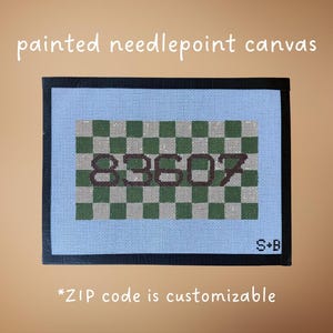 May include: Painted needlepoint canvas with a light blue background and a black border. The center features a green and white checkered pattern with the number "89607" in brown. The text "*ZIP code is customizable" is also present.