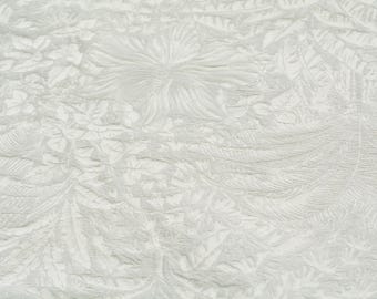 May include: Close-up of a white fabric with an embossed floral pattern. The design features stylized flowers and leaves, creating a textured surface. The fabric's color is a soft, off-white, suitable for various textile projects.